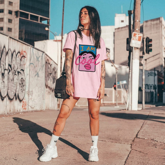 Woman wearing a pink t-shirt with a graphic design, standing on a street with graffiti in the background.
