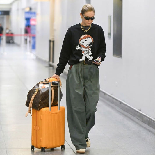 Person walking with luggage in a hallway, wearing a black sweater with a graphic design.