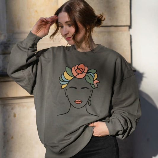 Woman wearing a gray sweatshirt with a colorful face design against a stone wall.