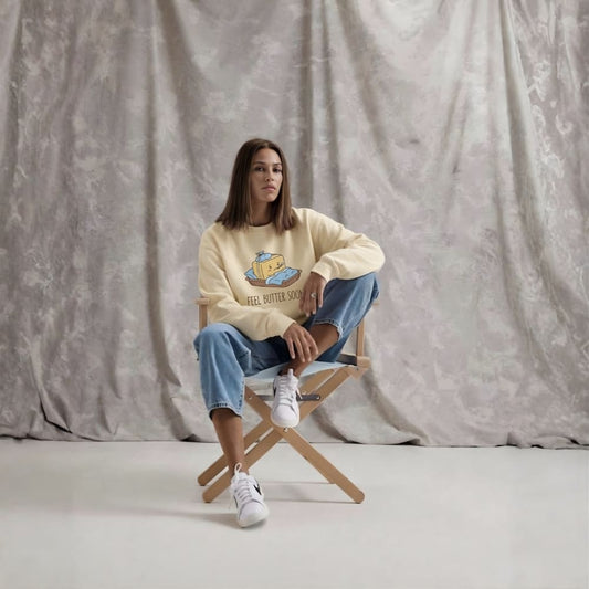 Person sitting on a chair wearing a beige sweatshirt with a graphic design against a plain background