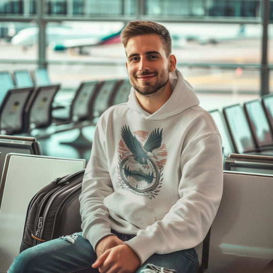 Man wearing a white hoodie with an eagle design, sitting in an airport terminal.