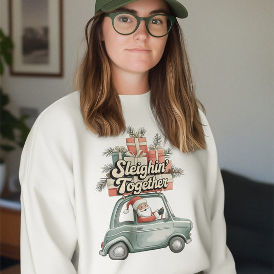 Person wearing a white sweatshirt with a Christmas design featuring Santa in a car and the text 'Sleighin Together'.