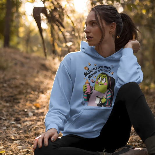 Woman wearing a light blue hoodie with a graphic design sitting in a forest.