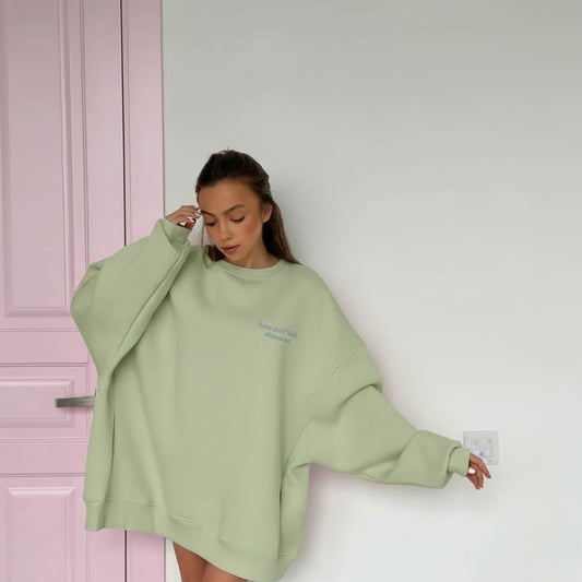 Person wearing a light green sweatshirt against a white wall with a pink door.
