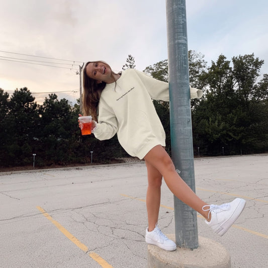 Person in a light-colored oversized sweater and white sneakers standing on a concrete block in an outdoor setting.