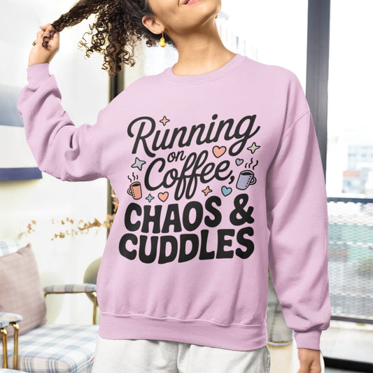 Person wearing a pink sweatshirt with text 'Running on Coffee, Chaos & Cuddles' in a casual setting.