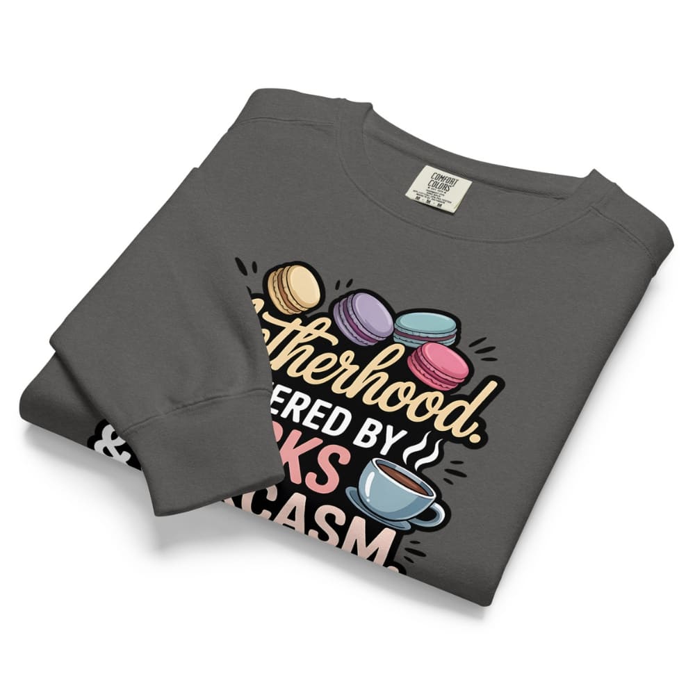 Sweatshirt design with text “Motherhood. Powered by Snacks & Sarcasm.” featuring colorful macarons and a steaming coffee cup on vintage-washed cotton fleece.