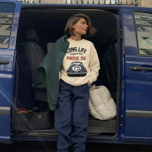 Person standing in the open trunk of a blue car wearing a sweatshirt with text and graphics.