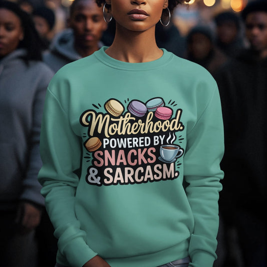 Sweatshirt design with text “Motherhood. Powered by Snacks & Sarcasm.” featuring colorful macarons and a steaming coffee cup on vintage-washed cotton fleece.
