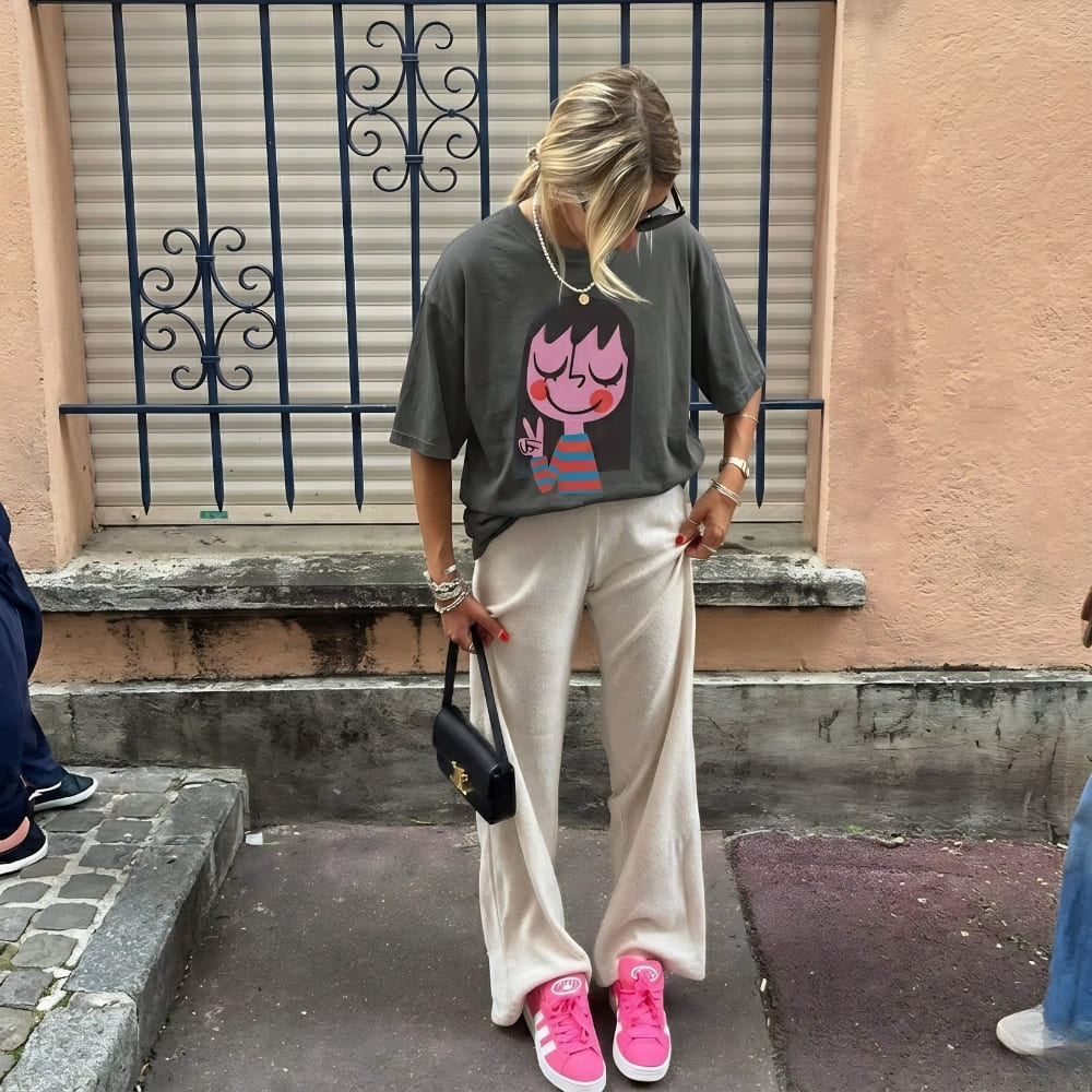 Person wearing a graphic t-shirt, beige pants, and pink sneakers on a street.