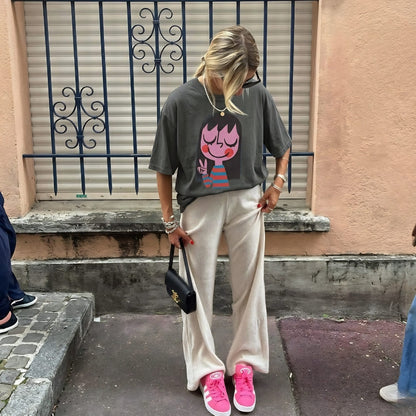 Person wearing a graphic t-shirt, beige pants, and pink sneakers on a street.