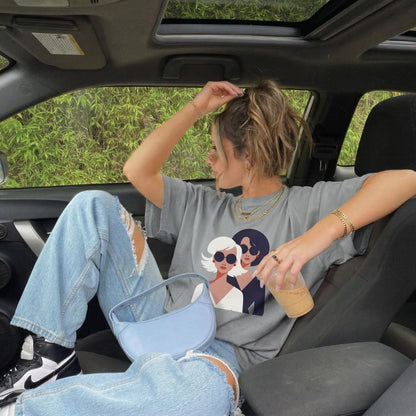 Person sitting in a car wearing a graphic t-shirt with two women on it.