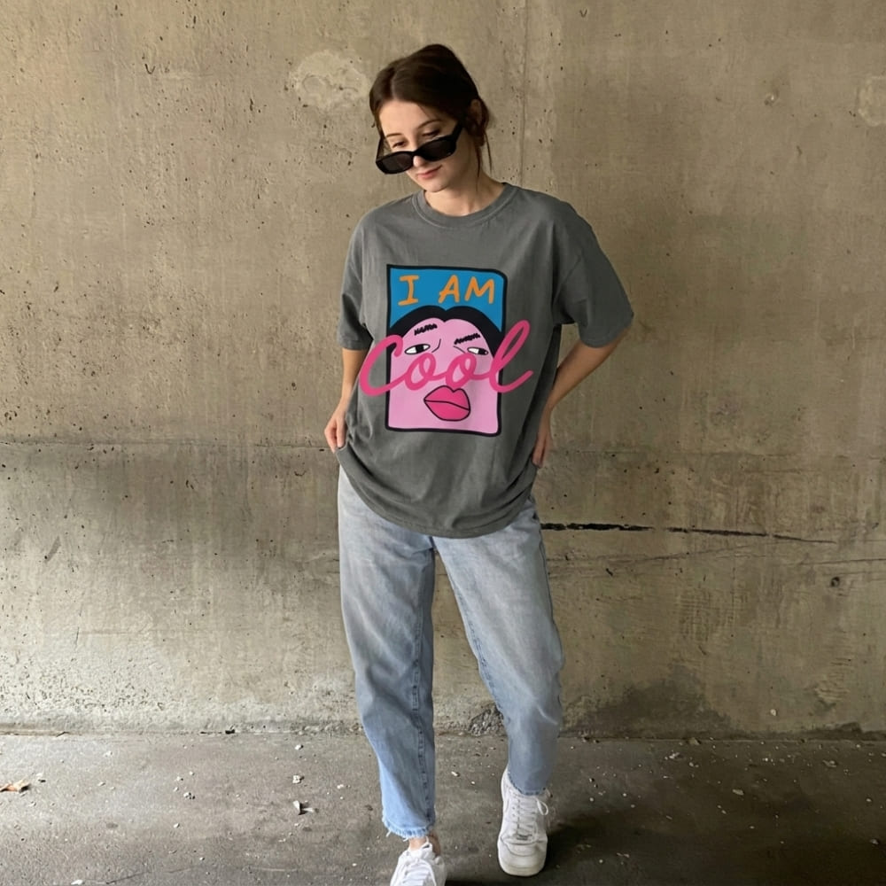 Person wearing a gray t-shirt with a colorful graphic design against a concrete wall.