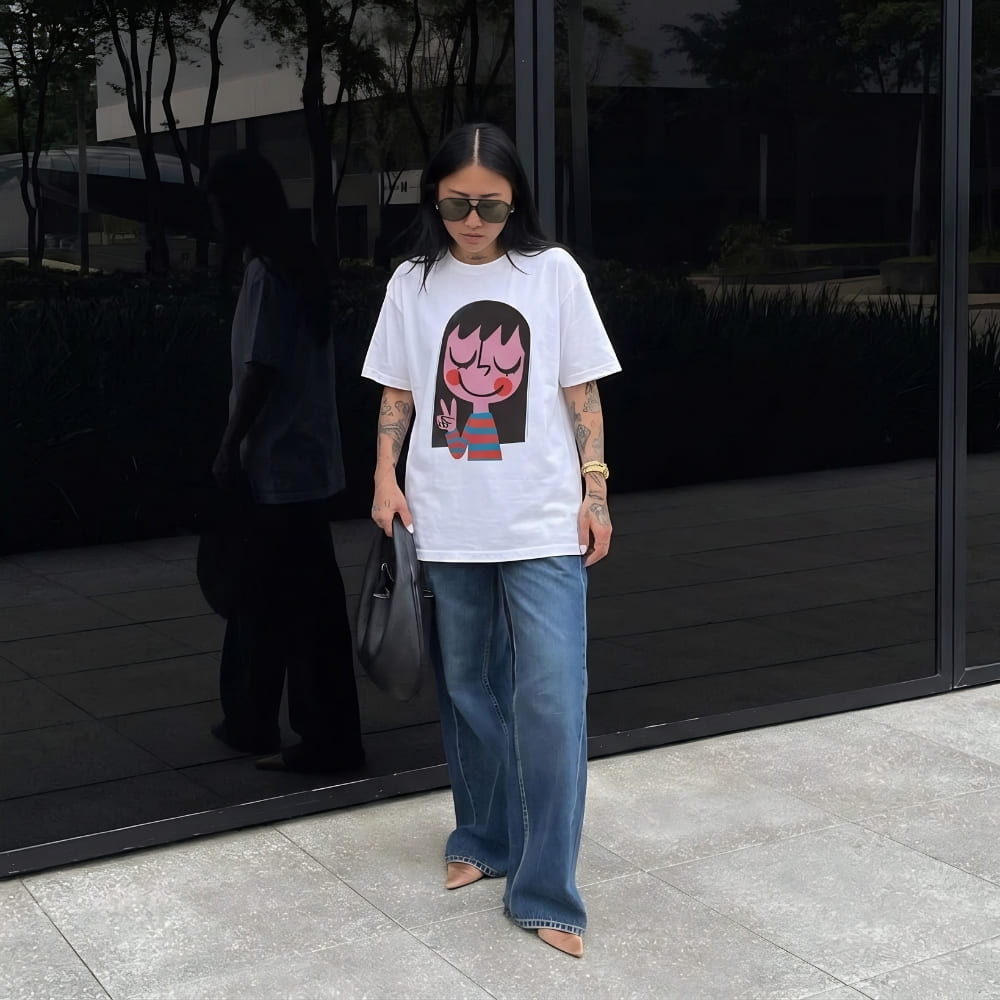 Person wearing a white t-shirt with a graphic design and blue jeans standing outdoors.