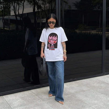 Person wearing a white t-shirt with a graphic design and blue jeans standing outdoors.