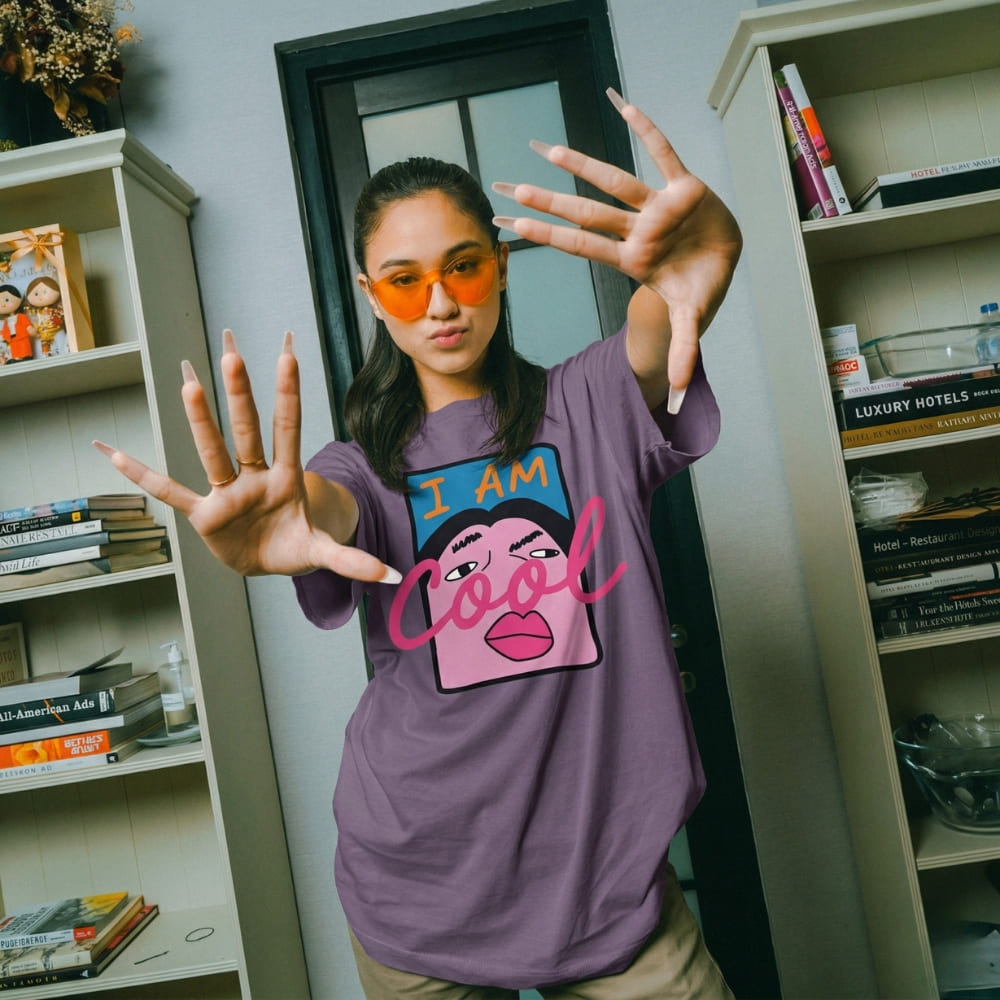 Person wearing a purple t-shirt with a graphic design and text, standing in a room with bookshelves.