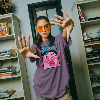 Person wearing a purple t-shirt with a graphic design and text, standing in a room with bookshelves.