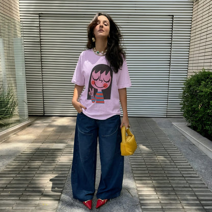 Woman wearing a pink t-shirt with a graphic design, blue jeans, and red shoes, standing outdoors.