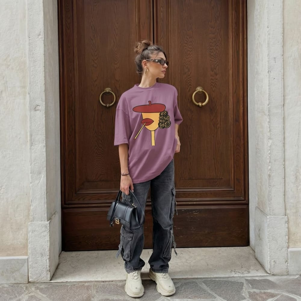 Person wearing a purple oversized t-shirt with a graphic design, standing in front of a wooden door.