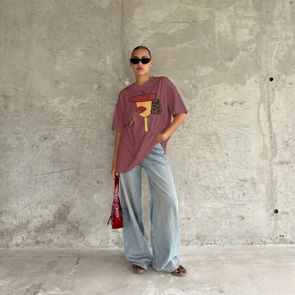 Person wearing a graphic t-shirt and light blue jeans against a concrete wall.