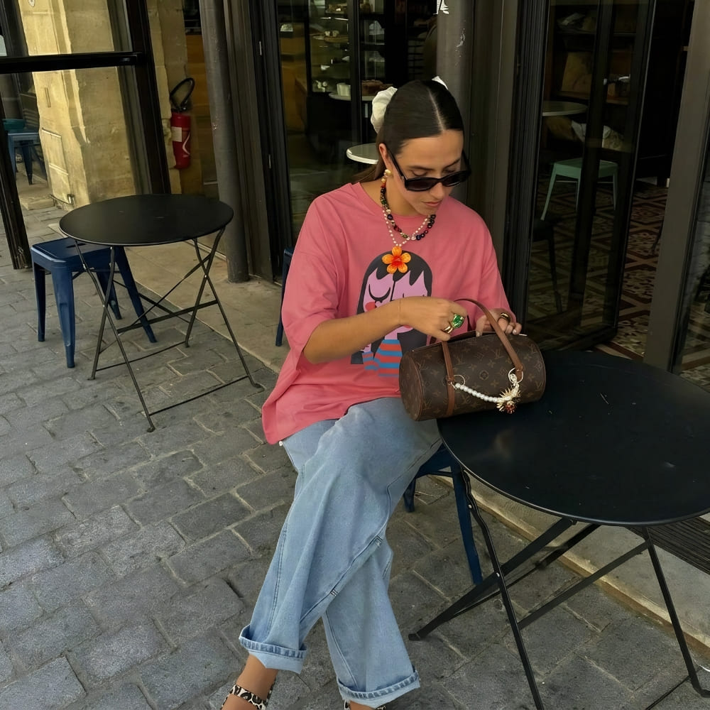 Person sitting at an outdoor cafe table holding a bag
