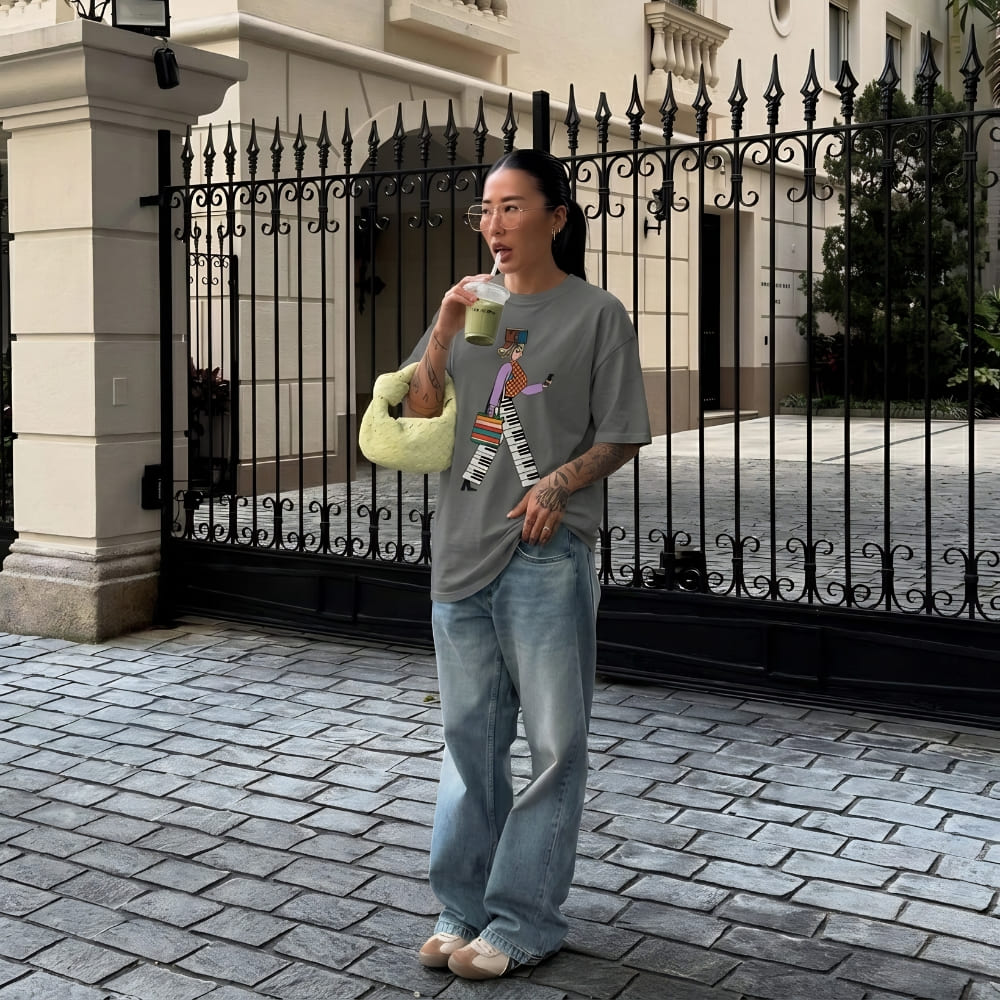 Person standing on a sidewalk in front of an iron gate, holding a drink.