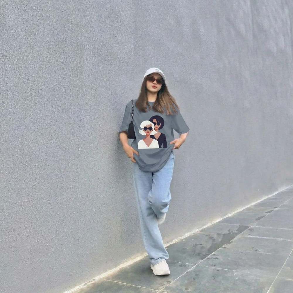 Person wearing a graphic t-shirt with a design of a woman and a cat, standing against a gray wall.