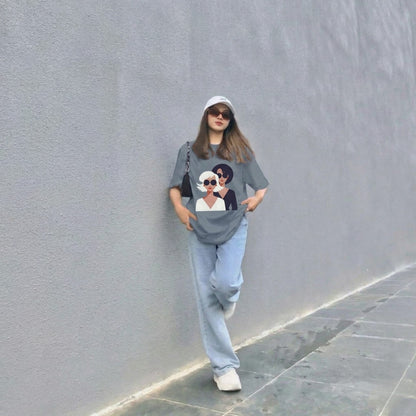 Person wearing a graphic t-shirt with a design of a woman and a cat, standing against a gray wall.