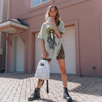 Woman holding a white backpack and a cup, standing in front of a house.