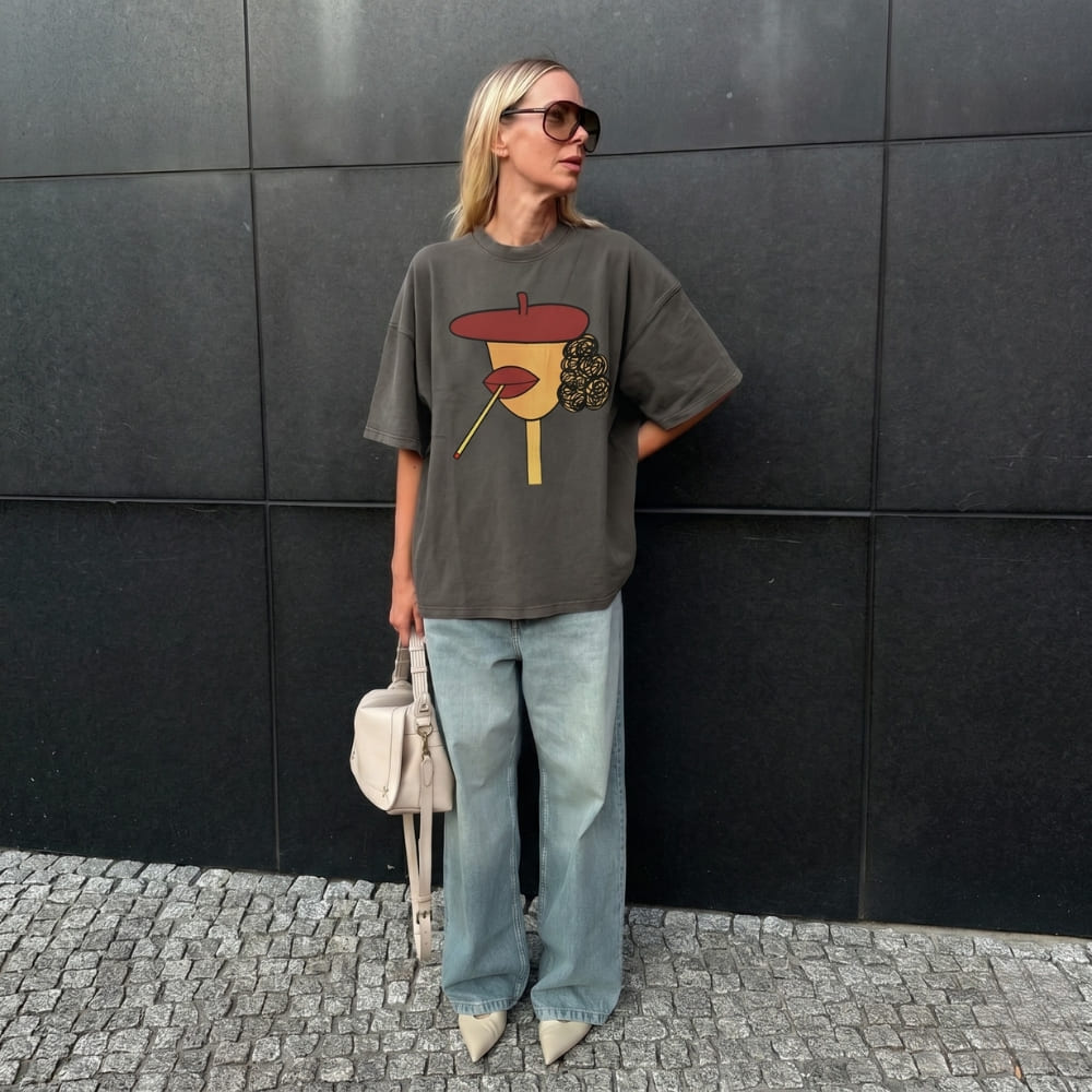 Person wearing a graphic t-shirt and jeans standing against a black wall.