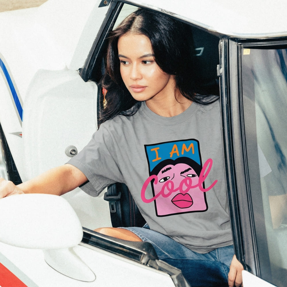 Woman sitting in a car wearing a gray t-shirt with a colorful graphic design.