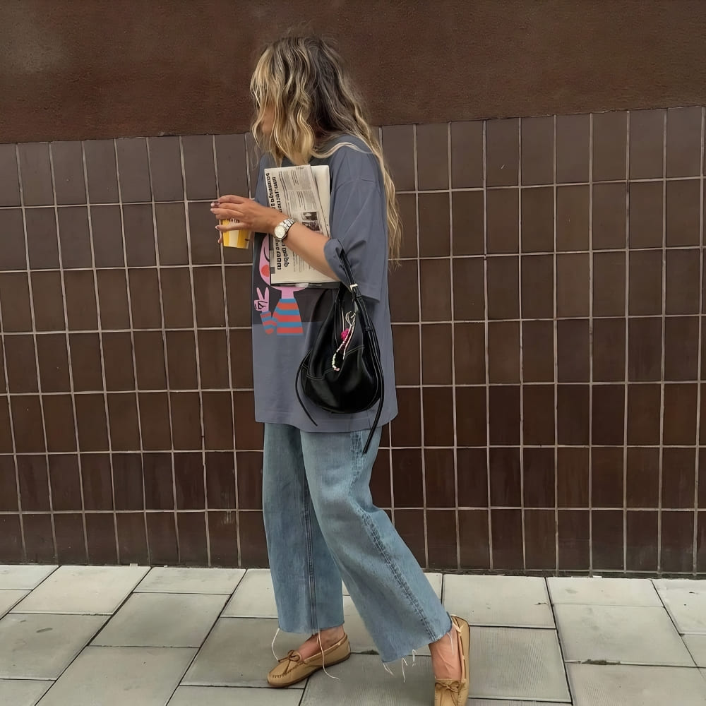 Person standing against a tiled wall holding a newspaper and a drink.