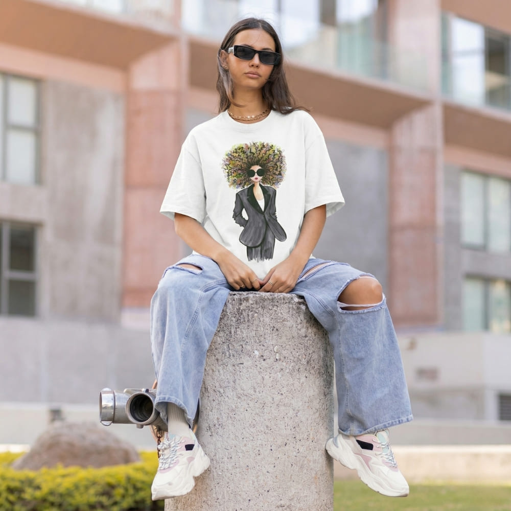 Person wearing a t-shirt with a graphic design of a person in a suit and sunglasses, sitting on a concrete block outdoors.