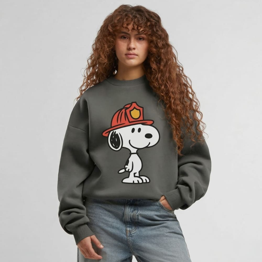 Person wearing a gray sweatshirt with a cartoon character and fire helmet design on a plain background