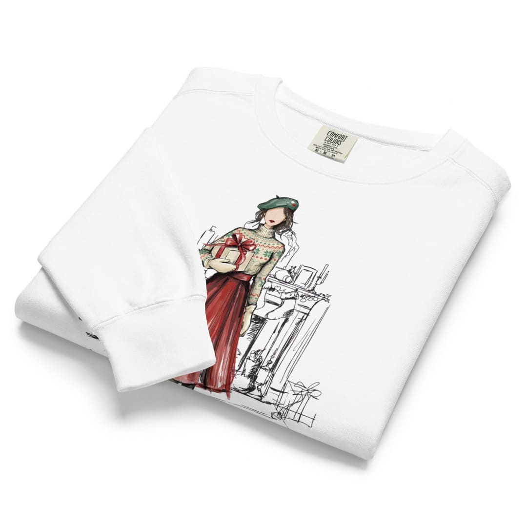 Holiday Muse™ sweatshirt by Blossombless.co in White, neatly folded to show the garment-dyed fleece and a sketch-style watercolor illustration of a faceless woman in a green beret, Fair Isle sweater and red pleated skirt holding a wrapped gift