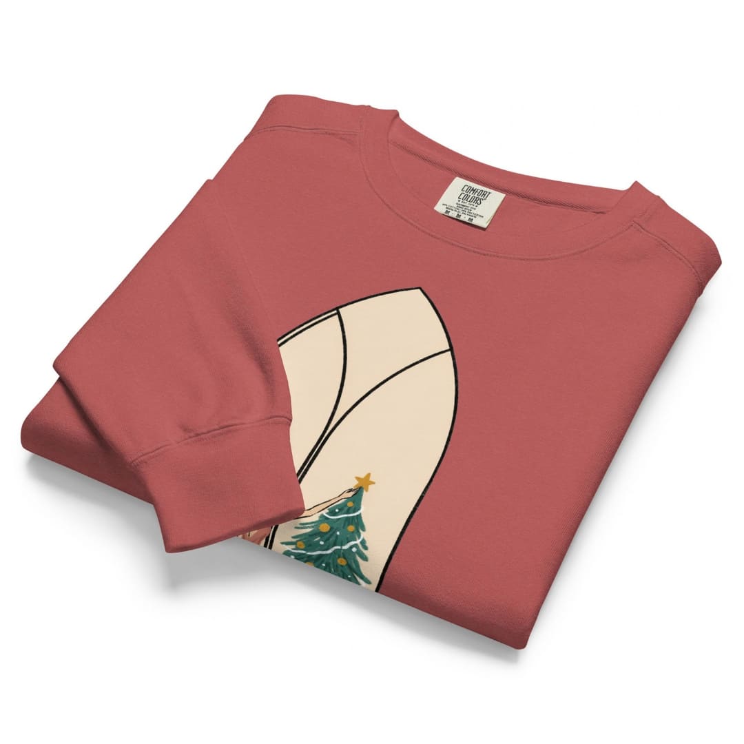 Star of the Season™ sweatshirt by Blossombless.co in Crimson, neatly folded to show the garment-dyed fleece and a soft pastel illustration of a woman in a backless rose gown placing a gold star on a Christmas tree, framed inside an ivory gothic arched window