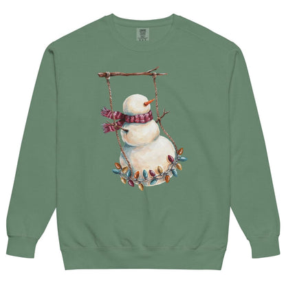 Swing Season™ sweatshirt by Blossombless.co in Light Green, front view: a painterly snowman swinging on a strand of vintage Christmas lights from a bare winter branch, wearing a striped burgundy scarf