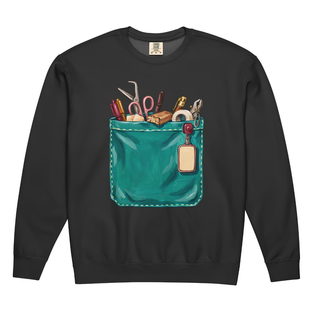 The Shift Pocket™ nurse sweatshirt in Black, front view: hand-painted teal scrub pocket holding trauma shears, a hemostat, pens, tape and a badge reel