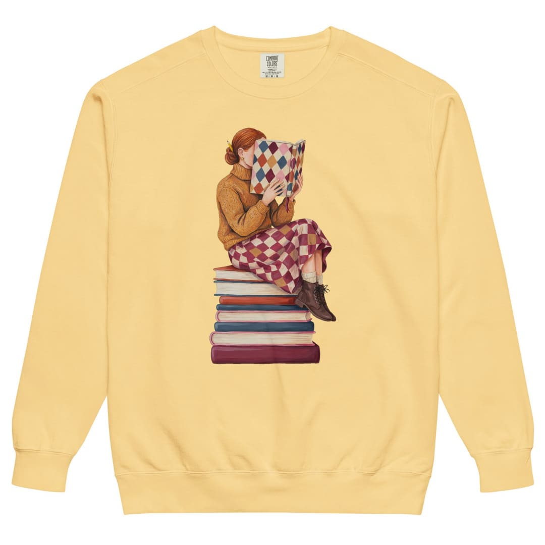 Between Chapters™ sweatshirt by Blossombless.co in Butter, front view: a painterly woman perched on a stack of books, her face hidden behind a harlequin hardcover
