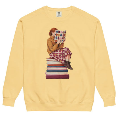 Between Chapters™ sweatshirt by Blossombless.co in Butter, front view: a painterly woman perched on a stack of books, her face hidden behind a harlequin hardcover