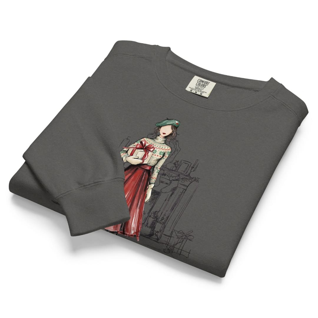 Holiday Muse™ sweatshirt by Blossombless.co in Pepper, neatly folded to show the garment-dyed fleece and a sketch-style watercolor illustration of a faceless woman in a green beret, Fair Isle sweater and red pleated skirt holding a wrapped gift
