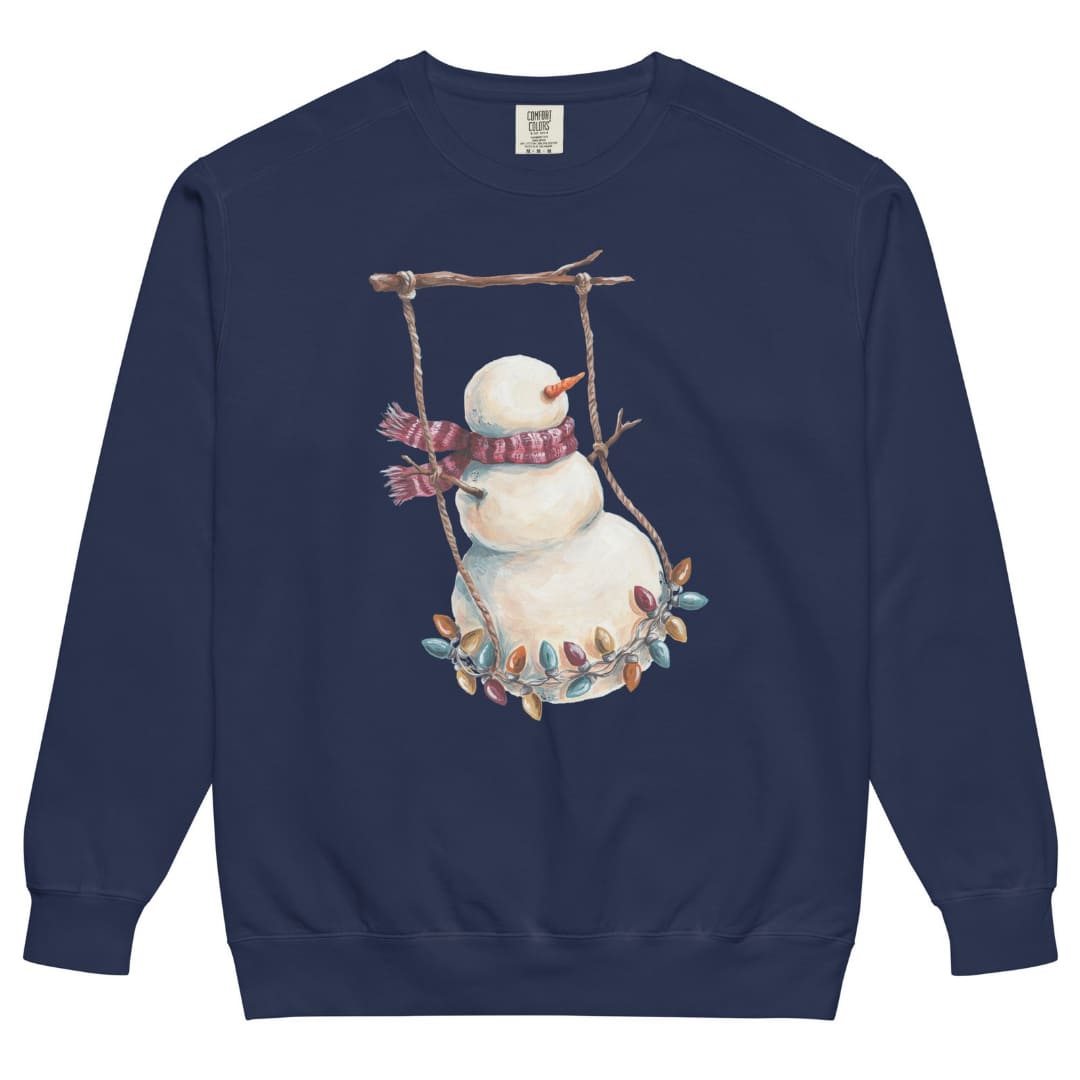 Swing Season™ sweatshirt by Blossombless.co in True Navy, front view: a painterly snowman swinging on a strand of vintage Christmas lights from a bare winter branch, wearing a striped burgundy scarf