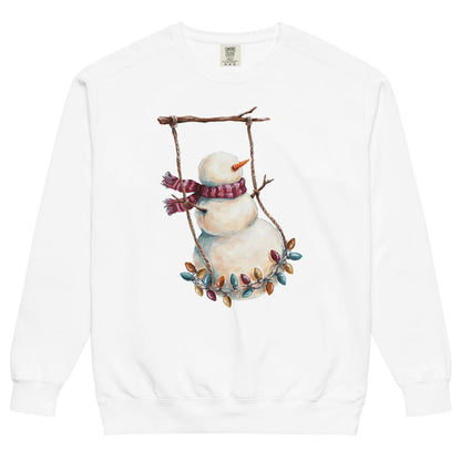 Swing Season™ sweatshirt by Blossombless.co in White, front view: a painterly snowman swinging on a strand of vintage Christmas lights from a bare winter branch, wearing a striped burgundy scarf