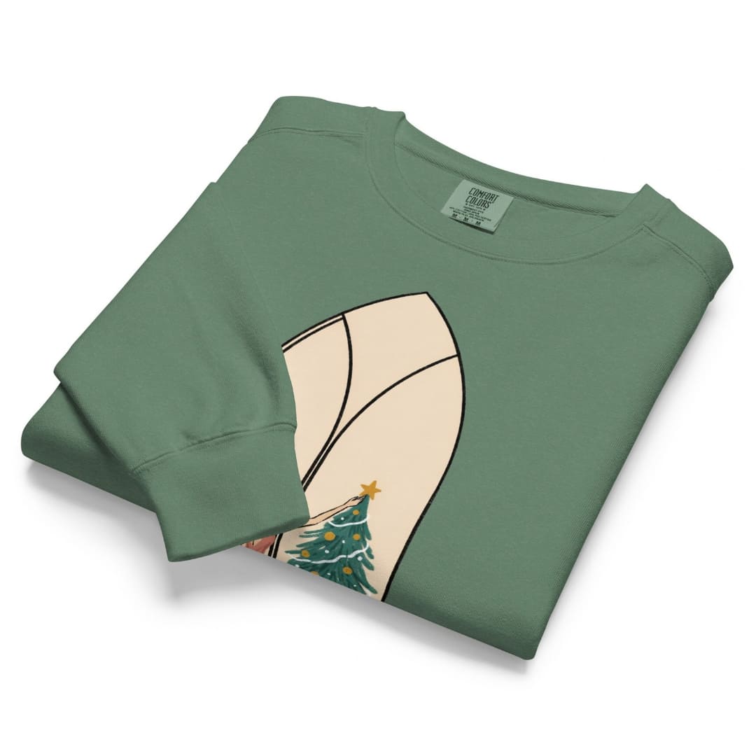 Star of the Season™ sweatshirt by Blossombless.co in Light Green, neatly folded to show the garment-dyed fleece and a soft pastel illustration of a woman in a backless rose gown placing a gold star on a Christmas tree, framed inside an ivory gothic arched window