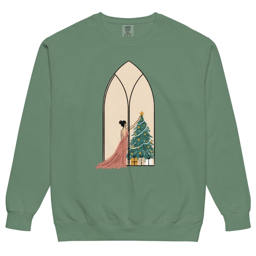 Star of the Season™ sweatshirt by Blossombless.co in Light Green, front view: a soft pastel illustration of a woman in a backless rose gown placing a gold star on a Christmas tree, framed inside an ivory gothic arched window
