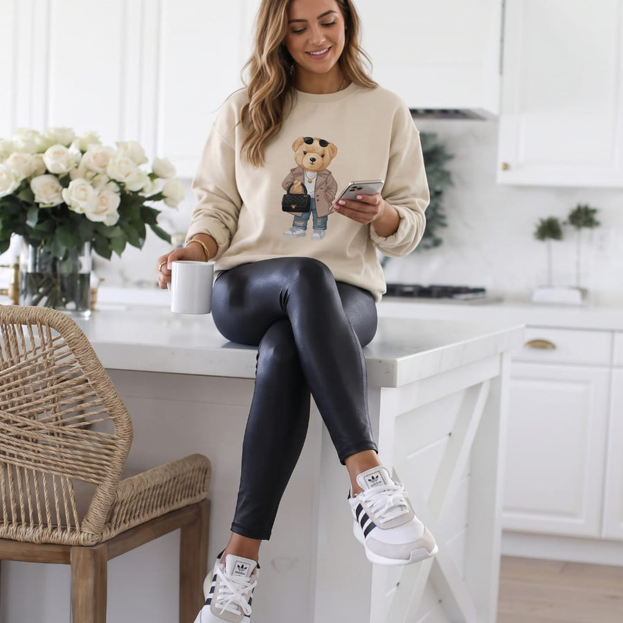 Miss Coco Belle™ oversized sweatshirt by Blossombless.co in Dust, lifestyle: woman in black leather pants seated in a bright white kitchen