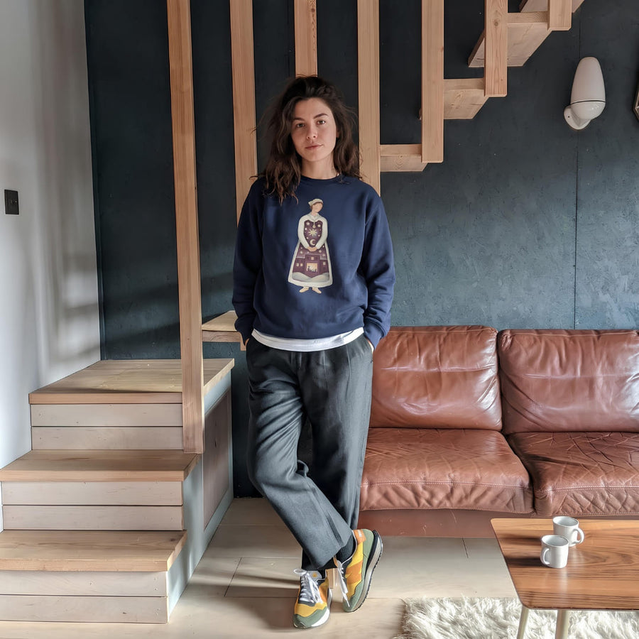 Woman in the Keeping Watch™ night shift nurse Christmas sweatshirt in True Navy, standing by a wooden staircase at home