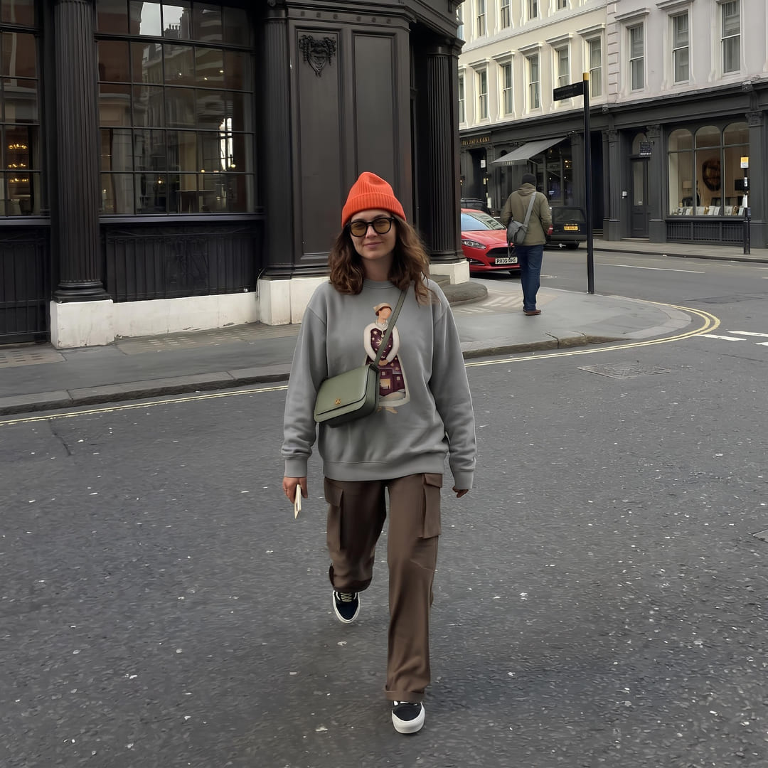 Woman crossing a city street in the Keeping Watch™ nurse sweatshirt in Grey and an orange beanie