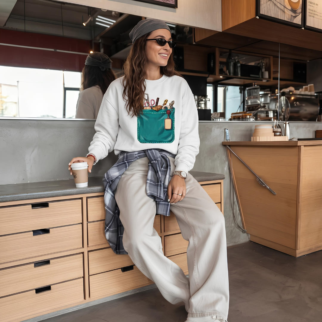 Woman wearing The Shift Pocket™ sweatshirt in White, leaning on a kitchen counter with a plaid shirt tied at the waist