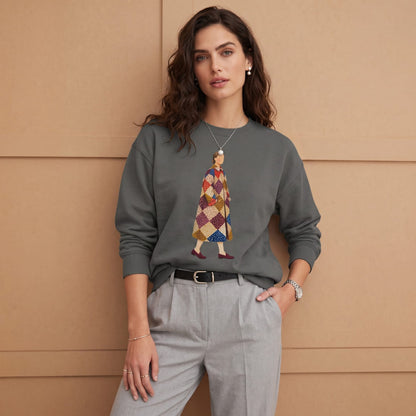 Woman wearing the Pieced Together™ sweatshirt by Blossombless.co in Pepper tucked into gray trousers with a black belt, standing against a warm wood-paneled wall